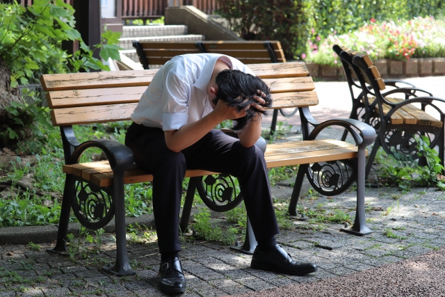 男性がベンチに座って頭を抱えている